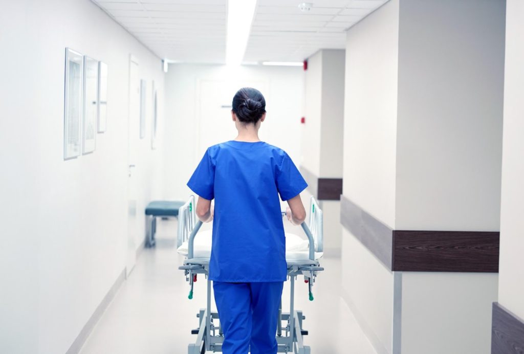 A nurse walking down a hallway, pushing a gurney in a hospital